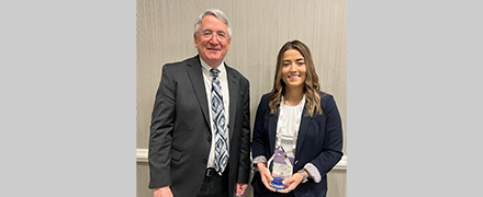 Photo shows a man in a suit presenting a research award to a young female surgeon.