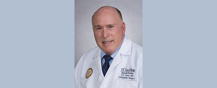 Photo of a surgeon wearing a white coat and looking at camera