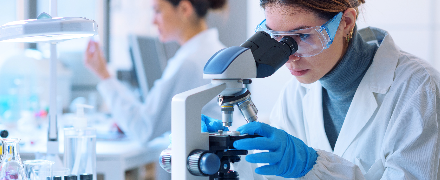 Woman in white lab coat looking through microscope