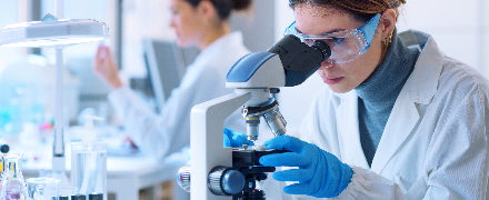 Woman-modern-microscope Woman in white lab coat looking through microscope